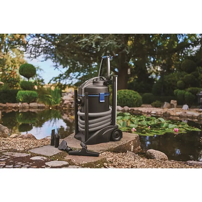Oase Teichschlammsauger PondoVac 3 - 1.600 W, 27 l - Schwarzer Teichsauger mit blauen Akzenten, geripptem Schlauch und Zubehör, auf einer Steinplatte neben einem Teich.