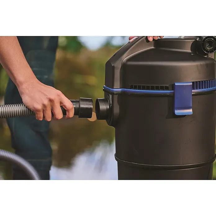 Oase Teichschlammsauger PondoVac 3 - 1.600 W, 27 l - Eine Person verbindet einen grauen Schlauch mit einem schwarzen Teichsauger mit blauen Akzenten, im Freien.