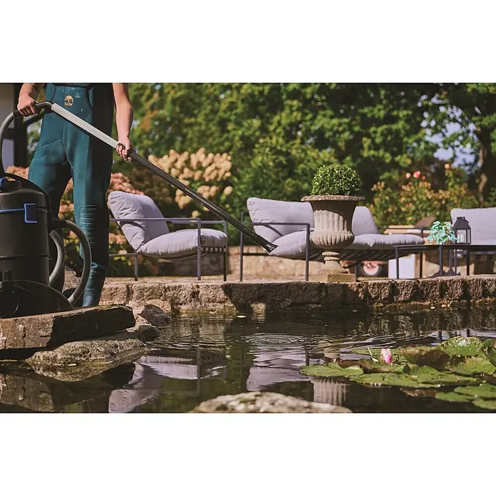 Oase Teichschlammsauger PondoVac 3 - 1.600 W, 27 l - Person in Wathose reinigt einen Gartenteich mit einem schwarzen Teichsauger und langer Reinigungsstange.