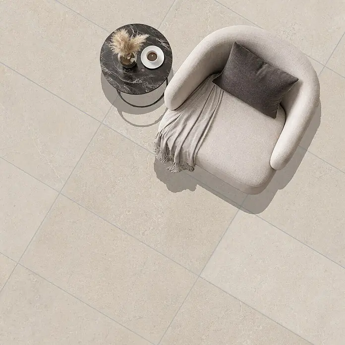 RAK Ceramics Feinsteinzeugfliese Valdi - 60 x 120 cm, White, Matt - Cremefarbene Bodenfliesen mit feiner Äderung, dünnen Fugen, diagonal verlegt. Ein Sessel und Beistelltisch stehen darauf.