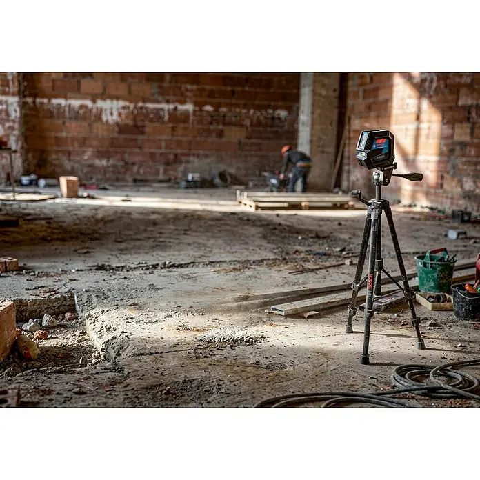 Bosch Professional Láser combinado GCL 2-50 - Zona de trabajo: 50 m (con receptor) - Un nivel láser Bosch negro y azul está montado en un trípode negro, instalado en una obra polvorienta, listo para trabajos de topografía.