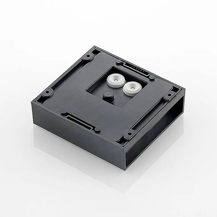 Lindby Außenwandleuchte Ugar - schwarz, schwarz, IP65 - Unterseite eines dunkelgrauen quadratischen Kunststoffgehäuses mit weißen Gummifüßen, einem zentralen schwarzen Stift und Anschlussleisten.