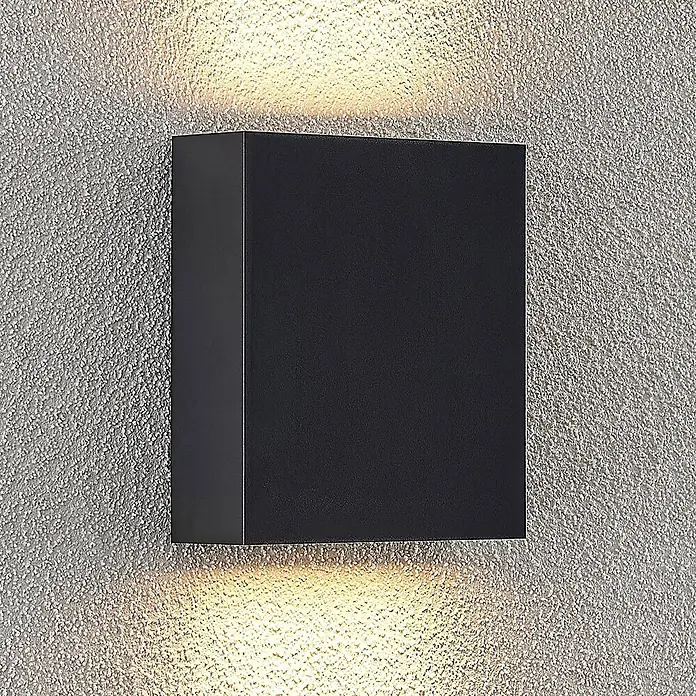 Lindby Außenwandleuchte Ugar - schwarz, schwarz, IP65 - Schwarze, rechteckige Außenwandleuchte, die warmes Licht nach oben und unten auf eine strukturierte Wand wirft.