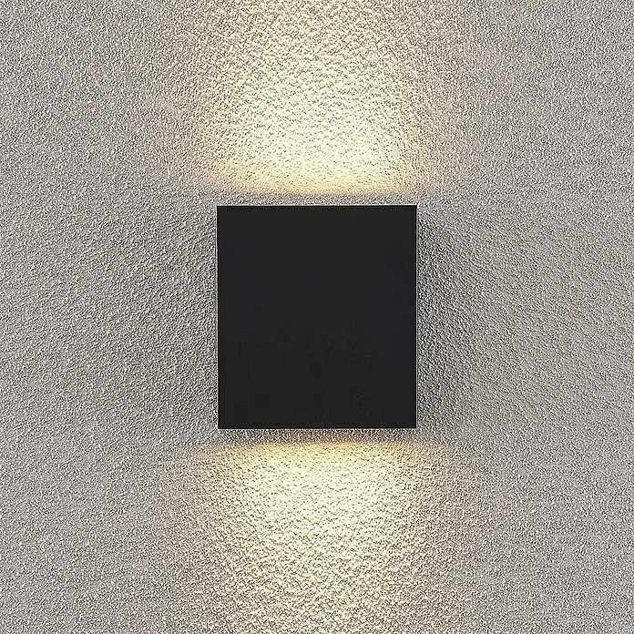 Lindby Außenwandleuchte Ugar - schwarz, schwarz, IP65 - Schwarze quadratische Wandleuchte beleuchtet eine strukturierte Wand mit warmen Auf- und Abwärtsstrahlen.