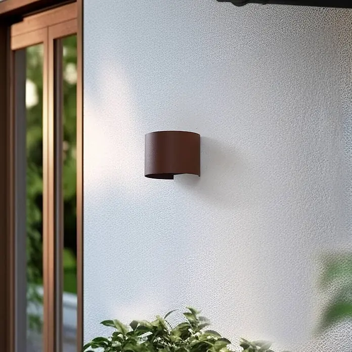 Lindby Außenwandleuchte Dara - braun / rost, IP54 - Braune zylindrische Wandleuchte an einer strukturierten Wand, die nach oben/unten leuchtet, neben einem Fenster.