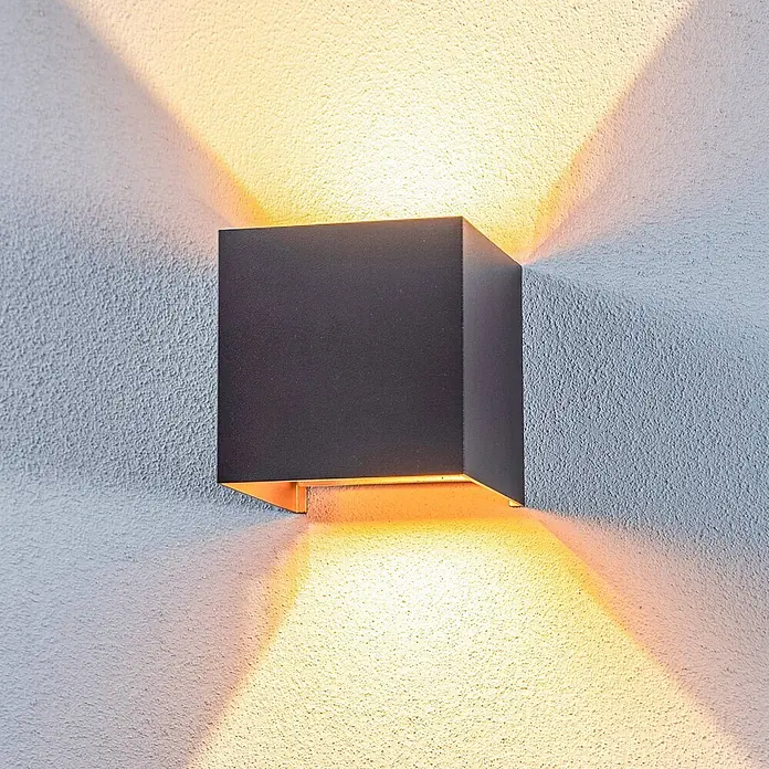 Lindby Außenwandleuchte Nivar - 10 x 10 x 10 cm, schwarz, IP54 - Dunkelgraue, kubische Wandleuchte wirft warmes Licht nach oben und unten auf eine strukturierte Wand.
