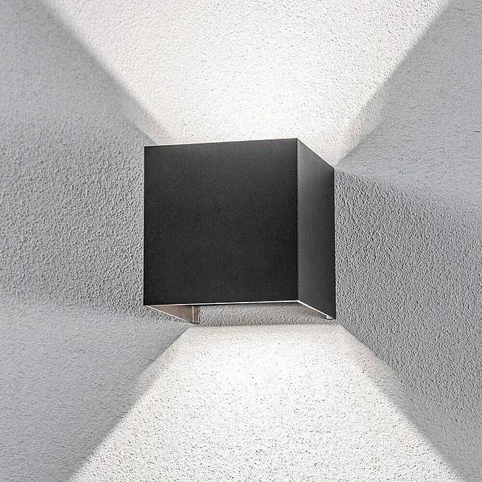 Lindby Außenwandleuchte Nivar - schwarz, IP54 - Schwarze kubische Wandleuchte an texturierter Wand, wirft Licht nach oben und unten in einem markanten Muster.