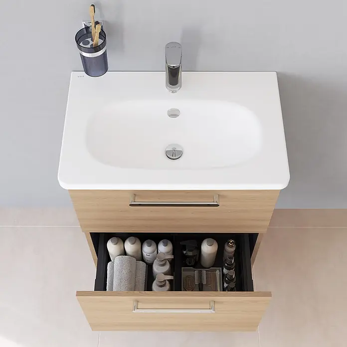 VitrA Root Flat Compact Badmöbel-Set Compact - B x T x H: 60 x 37 x 65 cm, Eiche Natur - Ansicht von oben auf einen modernen Waschtisch aus hellem Holz mit weißem Becken und geöffneter Schublade voller Pflegeprodukte.