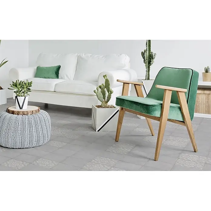 Feinsteinzeugfliese Triana - 24,8 x 24,8 cm, Flor Gris, Matt - Modernes Wohnzimmer mit weißem Sofa, grünem Samtsessel, grauem Strickhocker und Topfpflanzen.