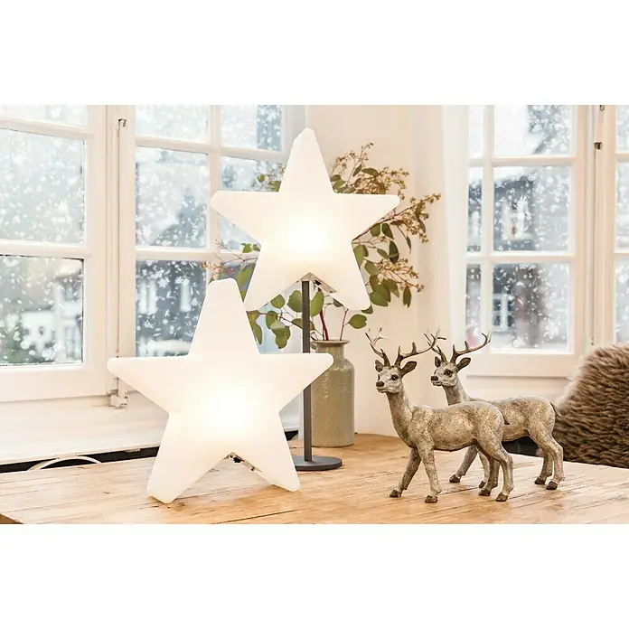 8 Seasons Design Shining LED-Stern Star - Außen, 10 cm, Neutralweiß - Dekorative Szene mit zwei leuchtenden Sternlampen und zwei Zierrehen auf einem Holztisch, vor einem Fenster mit Schnee.