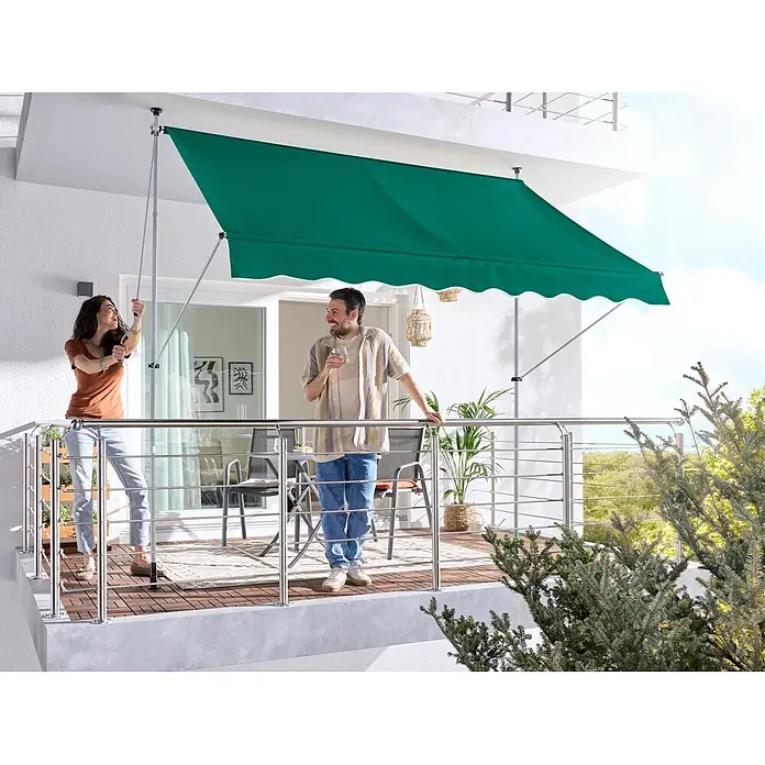 Sunfun Klemmmarkise - Grün, Breite: 3 m, Ausfall: 1,3 m - Grüne Stoff-Balkonmarkise spendet Schatten auf einem sonnigen Balkon, gestützt von verstellbaren Stangen, mit einem Paar, das den Raum genießt.