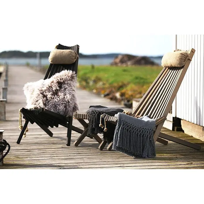 Jardinion Garten-Beistelltisch Abstelltisch 54cm x 49cm x 45cm Klapphocker Schwarz Kiefer - L x B x H: 54 x 49 x 45 cm, Schwarz - Zwei Holz-Liegestühle mit gemütlichen Kissen und Decken auf einer Holzterrasse mit Blick aufs Wasser, bereit zur Entspannung.
