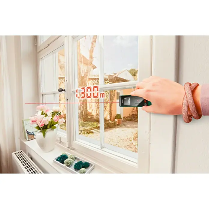 Bosch Medidor de distancia láser de bolsillo Zamo III - Gama de medición: 0,15 m - 20 m - Un medidor láser de distancia Bosch se utiliza para medir el ancho de una ventana, mostrando una pantalla digital.