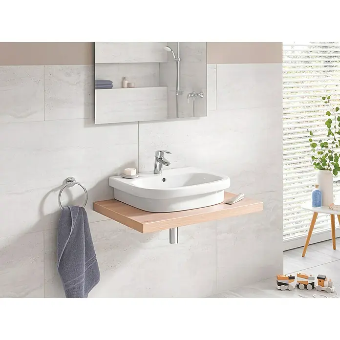 Grohe Eurosmart Grifo de lavabo - Cromo, Brillante, Con tirante, Arranque en agua fría - Primer plano de un baño moderno con un lavabo elegante sobre una estantería de madera, complementado con un toallero y un espejo.