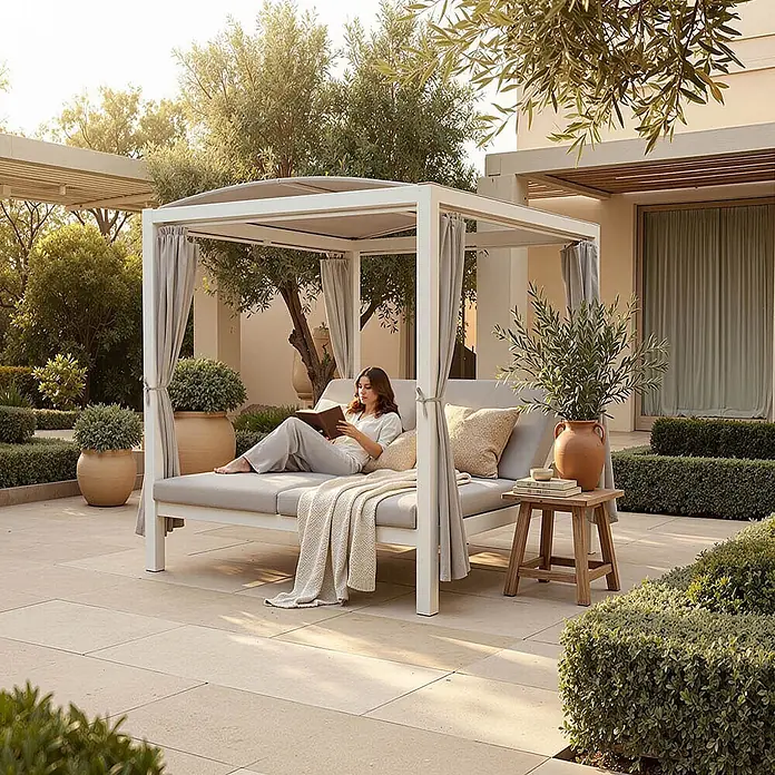 Home Deluxe Gartenliege LYON inkl. Abdeckung - B x T: 208 x 188 cm, Weiß, Grau, Polyester - Weißes Outdoor-Tagesbett mit Baldachin, hellgrauen Kissen und Vorhängen, auf dem eine Frau entspannt liest.