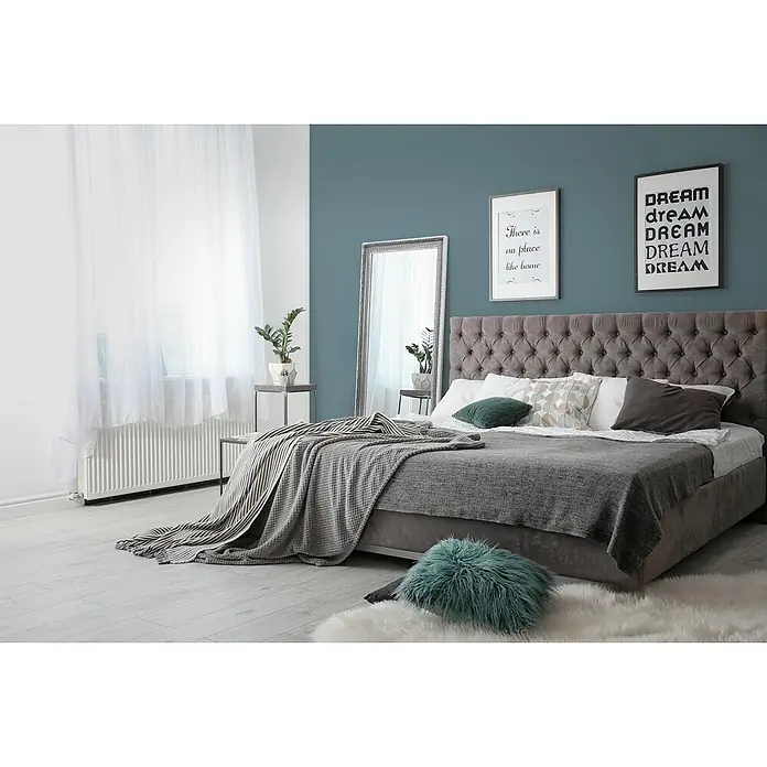 Livingwalls Wandfarbe Blau, Bluish Petrol DD125909 2,5l - Grün, Matt, 2,5 l - Graues Polsterbett mit getuftetem Kopfteil, geschichtetem grauem und gestreiftem Bettzeug sowie einem türkisfarbenen Akzentkissen.