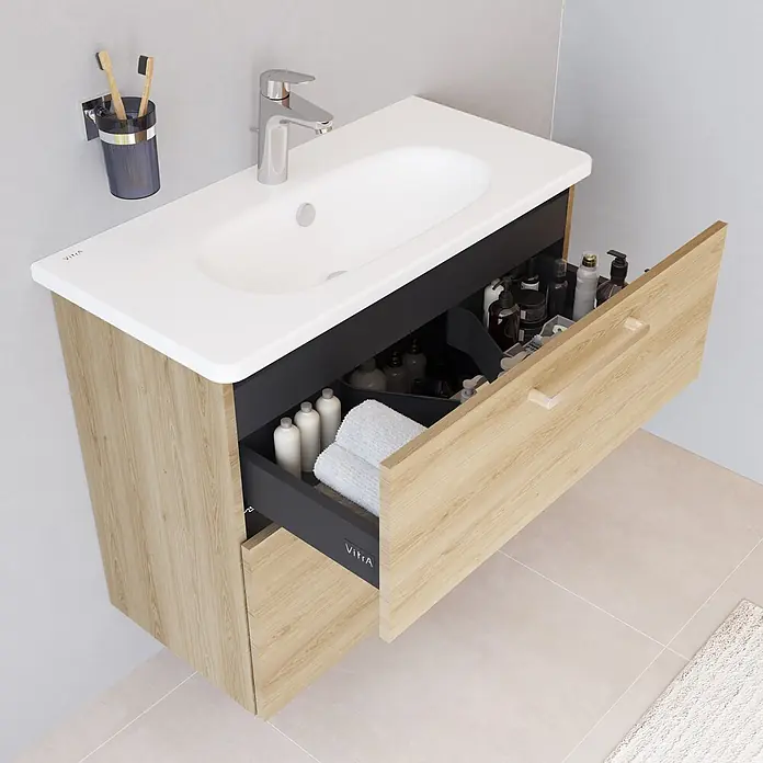 VitrA Root Flat Compact Badmöbel-Set Compact - B x T x H: 80 x 37 x 65 cm, Eiche Natur - Badezimmermöbel aus hellem Holz mit weißem Waschbecken, Chromarmatur und geöffneter dunkler Schublade mit Pflegeprodukten und Handtüchern.