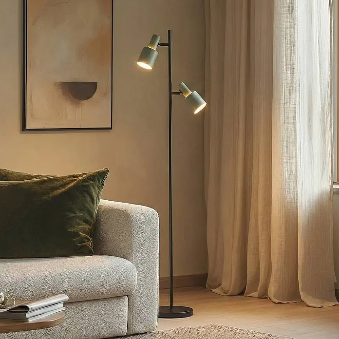 Lindby Stehleuchte Ovelia - Höhe: 155 cm, schwarz, grün, E27 - Moderne schwarze Stehlampe mit zwei grünen, verstellbaren Spotleuchten, die ein Wohnzimmer neben einem Sofa beleuchtet.