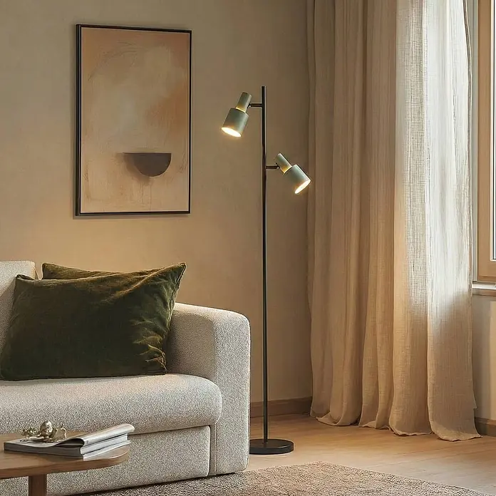 Lindby Stehleuchte Ovelia - Höhe: 155 cm, schwarz, grün, E27 - Schwarze Stehleuchte mit zwei verstellbaren hellolivgrünen Köpfen, die ein modernes Wohnzimmer neben einem Sofa beleuchtet.