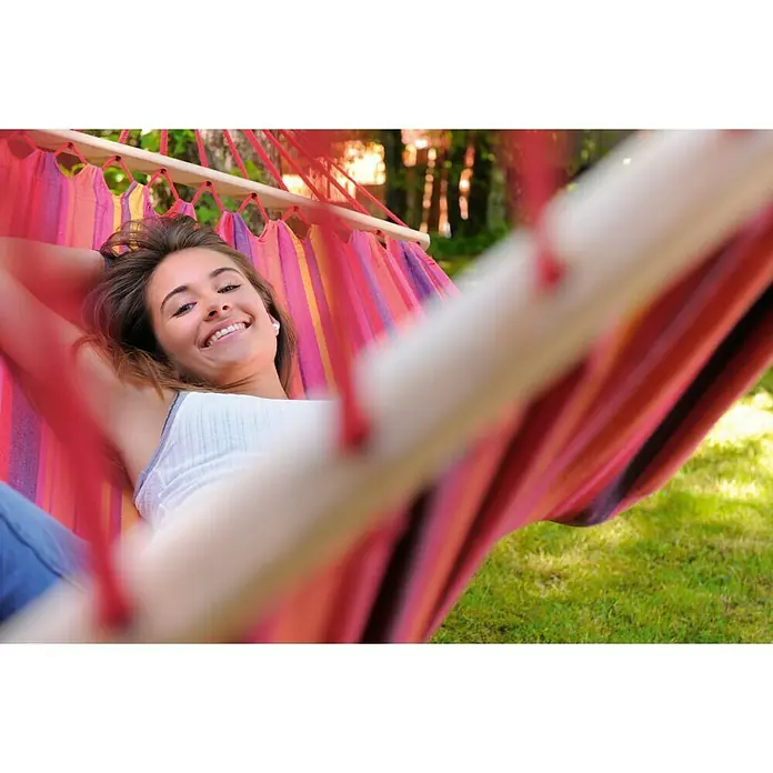 Amazonas Stabhängematte Tonga Vulcano - L x B: 310 x 100 cm, Rot/Orange/Gelb - Junge Frau entspannt in einer bunten Hängematte im Garten, die ein Gefühl von Sommerfreuden und Outdoor-Entspannung vermittelt.