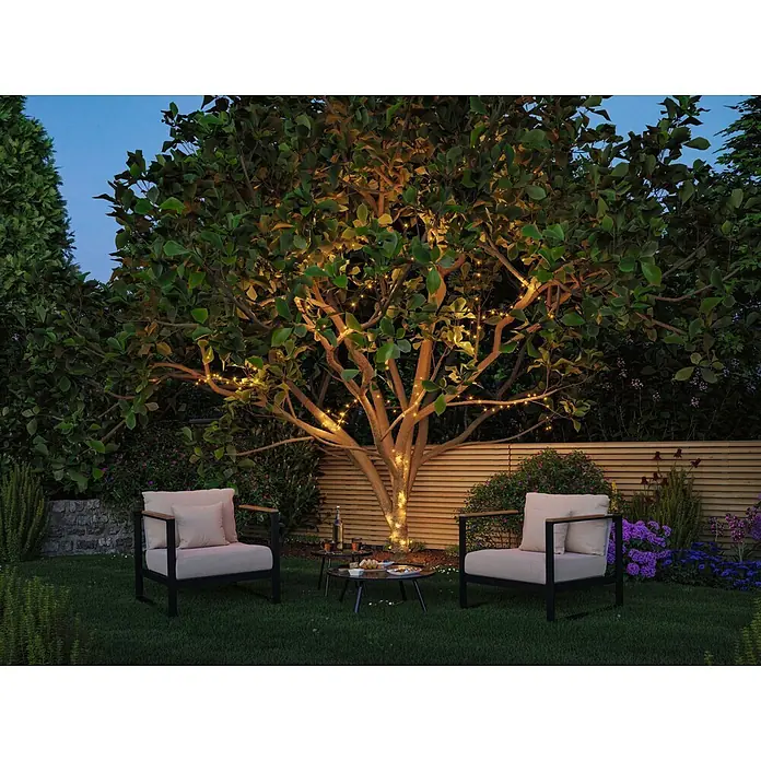 Paulmann Plug & Shine LED-Lichterkette Yuna - Außen, RGB, Länge: 7,4 m - Outdoor-Sitzgruppe: zwei schwarze Sessel mit hellen Kissen und ein kleiner Tisch in einem mit Lichterketten beleuchteten Garten.