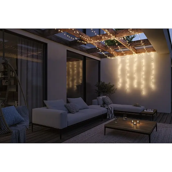 Paulmann Plug & Shine LED-Lichterkette Yuna - Außen, Warmweiß, Länge: 12,4 m - Warmweiße Lichterketten beleuchten eine Außenterrasse mit modernen Möbeln und schaffen eine gemütliche Abendatmosphäre an Pergola und Wand.