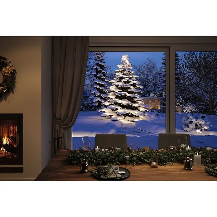 Paulmann Plug & Shine LED-Lichterkette Yuna - Außen, Warmweiß, Länge: 12,4 m - Ein gemütliches Weihnachtseszimmer mit festlich gedecktem Tisch, Kamin und Blick auf einen schneebedeckten Garten mit beleuchteten Bäumen in der Dämmerung.