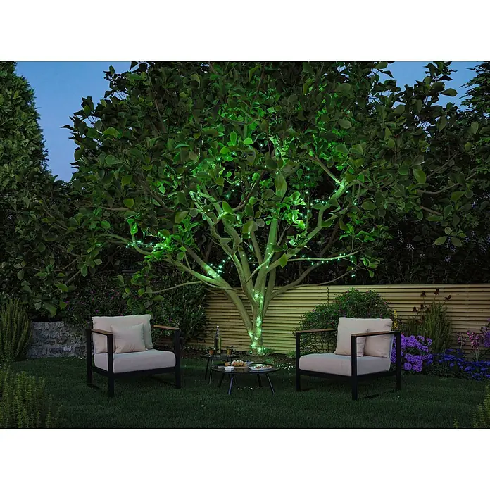 Paulmann Plug & Shine LED-Lichterkette Yuna - Außen, RGB, Länge: 7,4 m - Moderne Outdoor-Sessel mit schwarzen Gestellen, Holzarmlehnen und hellen Kissen, mit einem schwarzen Metalltisch im Garten.