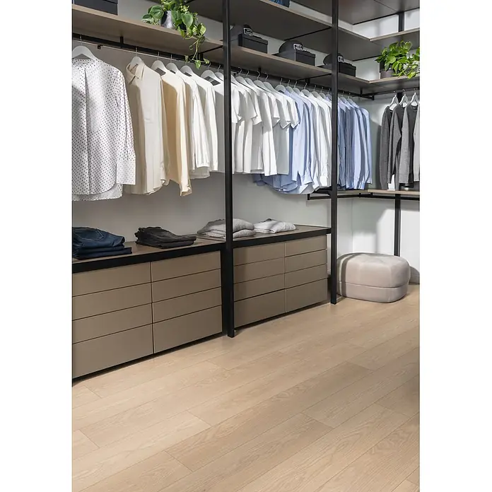 Egger Laminat NatureSense Promo - Baronia Eiche sand, Landhausdiele, 1.292 x 193 x 8 mm - Modernes begehbares Kleiderschranksystem mit taupefarbenen Schubladen, Regalen, schwarzem Metallrahmen und Kleiderstangen, mit Kleidung bestückt.
