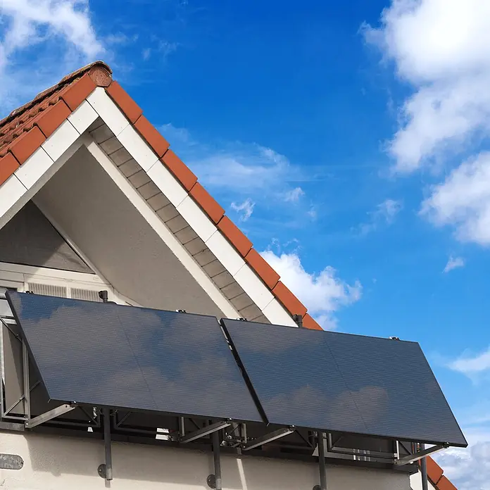 Sunniva Balkonkraftwerk-Set 1000 / 800 Watt mit BENY Wechselrichter - Nennleistung: 800 W, L x B x H: 1.906 x 1.134 x 30 mm - Zwei dunkle Solarmodule an der Fassade eines Gebäudes unter einem rot gedeckten Dach montiert.