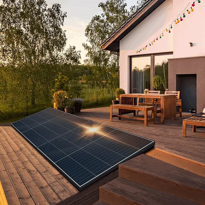 Sunniva Balkonkraftwerk-Set 920 / 800 Watt mit ECOFLOW Wechselrichter - Nennleistung: 800 W, L x B x H: 1.762 x 1.134 x 30 mm - Großes schwarzes Solarpanel auf einer Holzterrasse neben einem Haus, das die Sonne reflektiert.