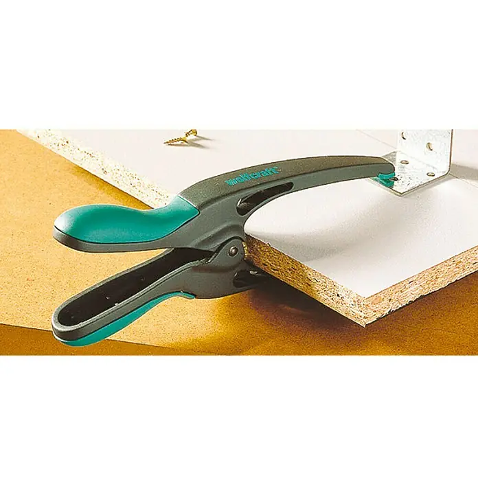 Wolfcraft Federzwinge MT 70 - Spannweite: 70 mm, Ausladung: 70 mm - Bild einer Wolfcraft Einhandzwinge, die zwei Holzplatten fixiert. Das Werkzeug ist grau mit türkisfarbenen Akzenten und erleichtert die Montage.
