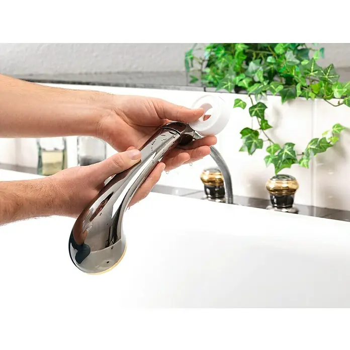Tesa Cinta Stop Water - Blanco, 12 m x 12 mm - La imagen muestra una ducha de mano sostenida por dos manos, fijándola a un grifo con un anillo blanco.