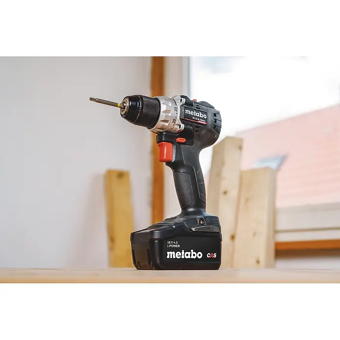Metabo CAS 18V Akku-Bohrschrauber BS 18 Black Edition - 18 V, 1 Akku, 4 Ah, 60 Nm - Schwarze und silberne Metabo Akku-Bohrmaschine mit Schraubendreher-Bit, stehend auf einer Holzoberfläche in einer Werkstatt.