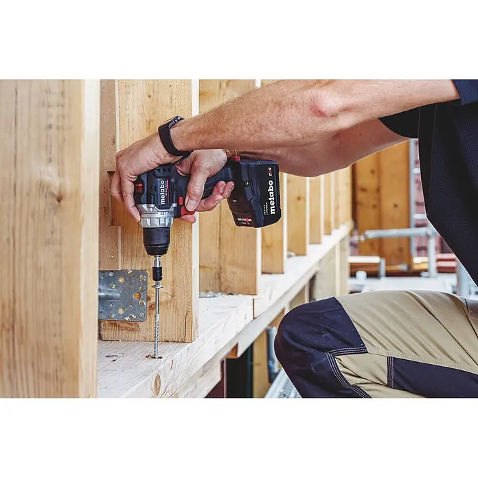 Metabo CAS 18V Akku-Bohrschrauber BS 18 Black Edition - 18 V, 1 Akku, 4 Ah, 60 Nm - Eine Person verwendet einen schwarz-silbernen Metabo Akku-Bohrschrauber, um eine lange Schraube in einen Holzrahmen zu drehen.