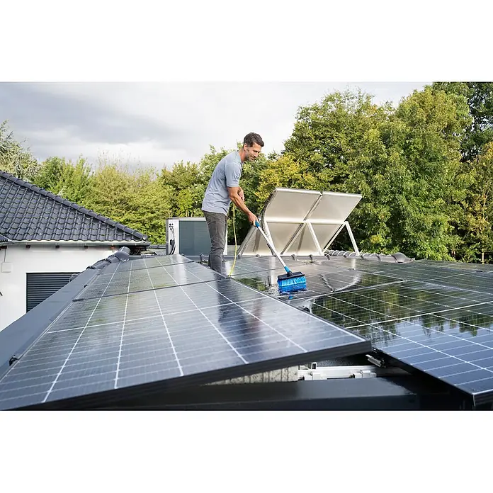 Unger HighFlow Reinigungs-Set Reinwasser 1,2m - 3 -tlg. - Mann reinigt Solarpanels auf einem Dach mit einer langstieligen Bürste mit blauen Borsten.
