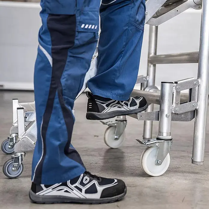 Munk Stehleiter Montageplattform mit Treppenzustieg 3m AH - Anzahl Tritte: 3 Stk., Arbeitshöhe: 3.000 m, Aluminium - Aluminium-Rollgerüst mit robusten Rollen, von Person in Arbeitskleidung genutzt.