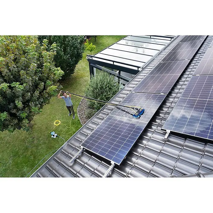 Unger HighFlow Reinigungs-Set Reinwasser 6m - 4 -tlg. - Mann reinigt Solarmodule auf dem Dach mit einem langen, wasserführenden Bürstensystem, das an einen Schlauch angeschlossen ist.