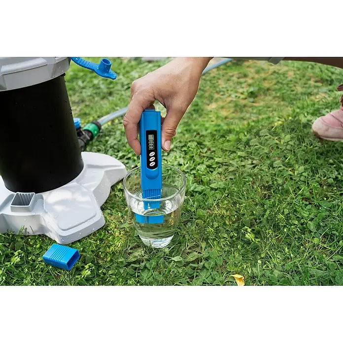 Unger HighFlow Filter Reinwasser - Passend für: Unger HighFlow Reinigungs-Set Komplettstange - Hand hält blaues TDS-Messgerät in Wasserglas, misst Reinheit im Freien neben Wasserfilter.