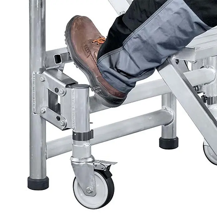 Zarges Stehleiter Montageplattform Workmaster T 2,70x0,75m klappbar - Anzahl Tritte: 3 Stk., Arbeitshöhe: 3.000 m, Aluminium - Arbeiterstiefel betätigt die schwarze Bremse an einer silbernen Gerüstrolle.