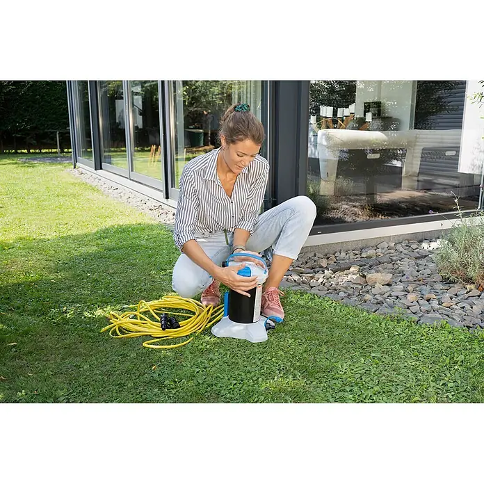 Unger HighFlow Filter Reinwasser - Passend für: Unger HighFlow Reinigungs-Set Komplettstange - Frau stellt kompakte, tragbare schwarz-weiße Pumpe mit blauen Akzenten im Garten auf, gelber Schlauch in der Nähe.
