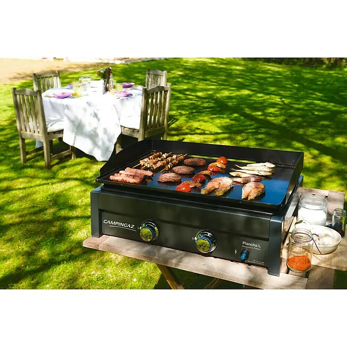Campingaz Barbacoa de gas L - Superficie de la parrilla (An x Pr): 66 x 42 cm, Número de quemadores: 2 - La imagen muestra una parrilla CampinGaz Plancha L con varios alimentos cocinándose, ideal para experiencias de cocina al aire libre.