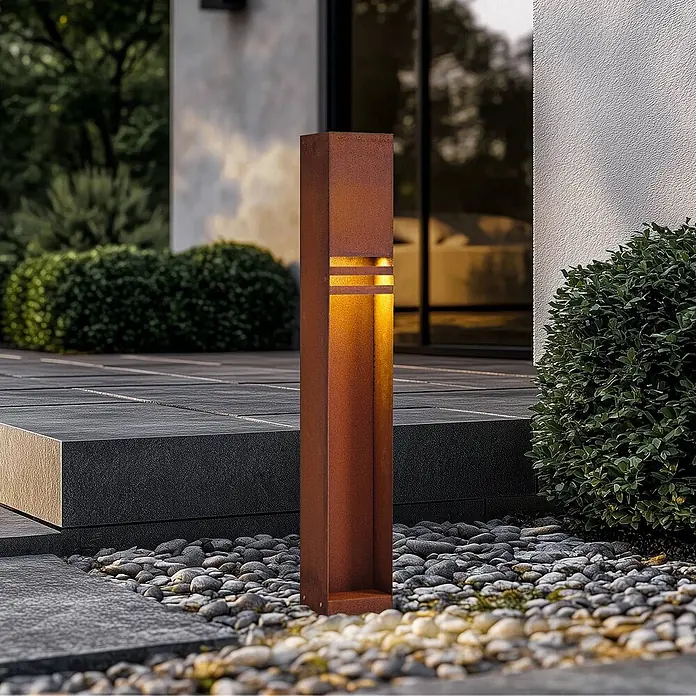 Lucande Außenlaterne Oxido -  - Rostfarbene Cortenstahl-Pollerleuchte für den Außenbereich mit warmer Beleuchtung auf einem Gartenweg mit Kieseln.