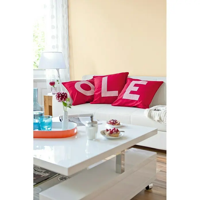 SCHÖNER WOHNEN-Farbe MyColour Wandfarbe - Sisal, Matt, 5 l - Dekoratives Wohnzimmer mit einem eleganten weißen Couchtisch, roten Kissen und einer weißen Couch, die eine gemütliche Atmosphäre schaffen.