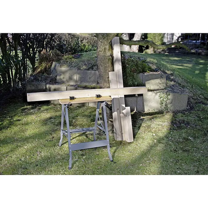 Werkbank Klappbar - L x B: 63,5 x 60,6 cm, Arbeitshöhe: 76 cm, Belastbarkeit: 150 kg - Blick auf eine graue Werkbank im Freien mit Holzbrettern darauf, die sich ideal für Bau- und Heimwerkerprojekte eignen.