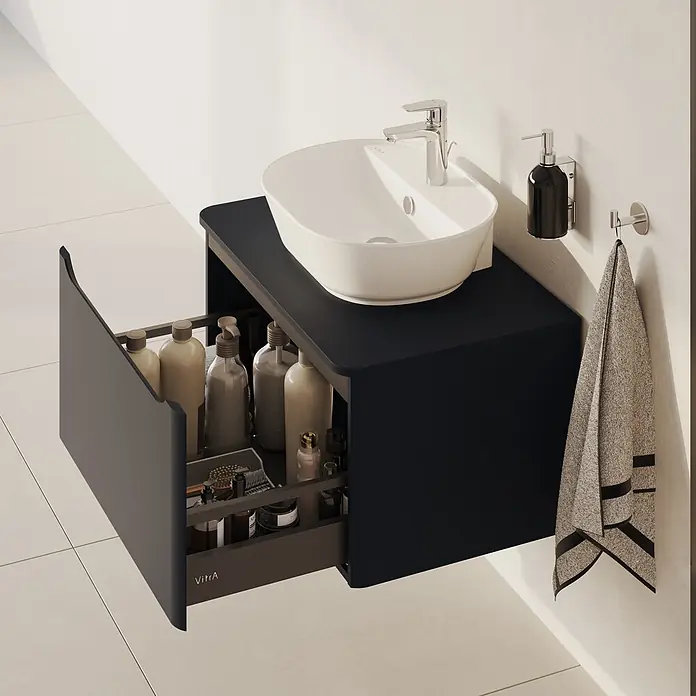 VitrA Integra Round Waschtischunterschrank Integra Round - B x T x H: 76,5 x 52 x 42 cm, Graphit - Wandmontierter schwarzer Badunterschrank mit weißem Aufsatzwaschbecken, Chromarmatur und geöffneter Schublade mit Pflegeprodukten. Ein Handtuch hängt daneben.