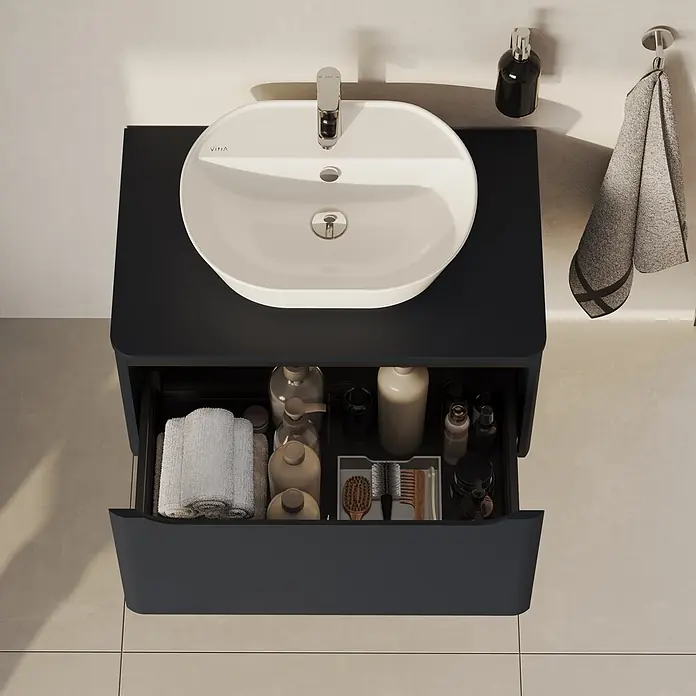 VitrA Integra Round Waschtischunterschrank Integra Round - B x T x H: 76,5 x 52 x 42 cm, Graphit - Dunkelgrauer schwebender Waschtisch mit weißem Waschbecken und offener Schublade, gefüllt mit Pflegeprodukten und Handtüchern.