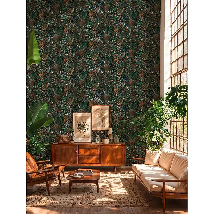 A.S. Création Cuba 2 Vliestapete Ethno - Grün-Braun, Floral, 10,05 x 0,53 m - Detailreiche Mustertapete in Dunkelgrün, Blau und Orange bedeckt eine Wand in einem sonnigen Wohnzimmer mit Pflanzen und Holzmöbeln.