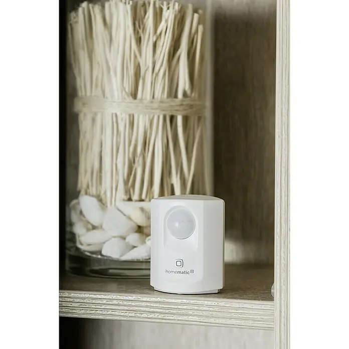 Homematic IP Funk-Bewegungsmelder HmIP-SMI - Weiß, 34 x 52 x 65 mm, Batteriebetrieben - Das Bild zeigt einen Homematic IP Bewegungsmelder in Weiß, platziert auf einem Regal mit dekorativen Elementen im Hintergrund.