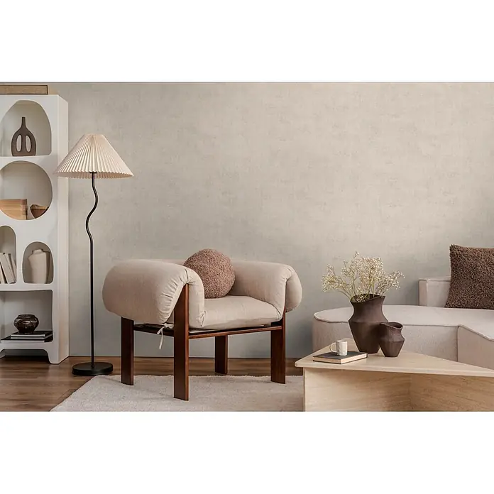 A.S. Création Nordic Feeling Vliestapete Uni - Grau-Grün, Uni, 10,05 x 0,53 m - Hellbeiger Stoff-Sessel mit dunklem Holzrahmen und weicher Polsterung, mit braunem Kissen in einem gemütlichen Wohnzimmer.